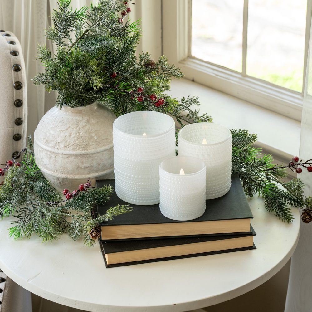 White hobnail glass flameless candles on books with greenery beside a cream vase